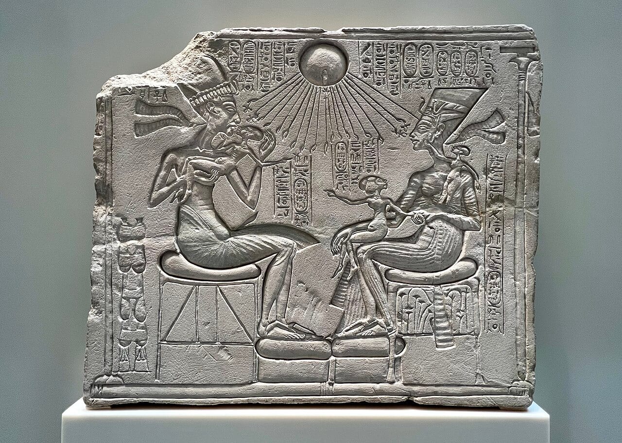 Relief sculpté d'une famille royale assise sous un disque solaire aux rayons terminés par des mains