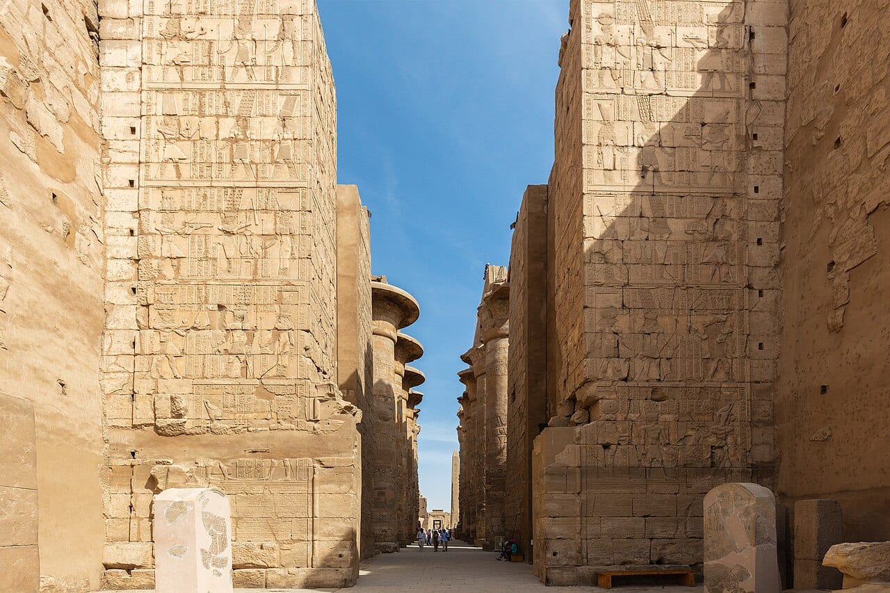 Longue allée bordée de hauts murs de pierre dans le temple de Karnak