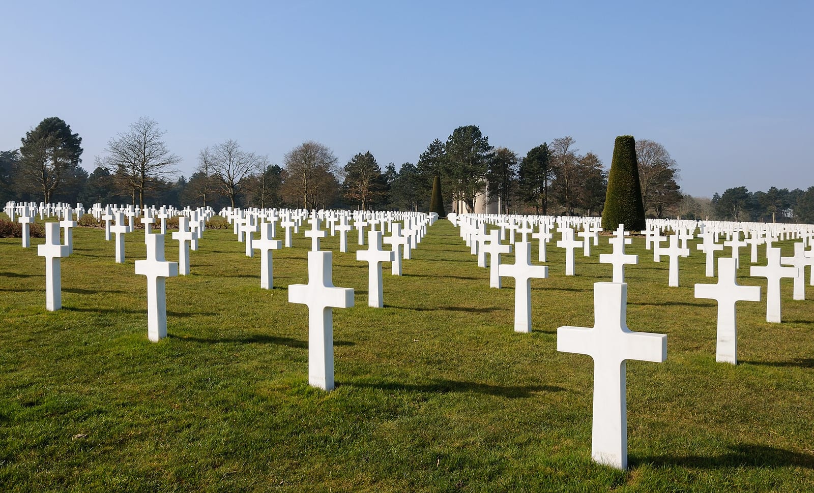 Rangées de croix blanches alignées sur une pelouse, sous un ciel bleu