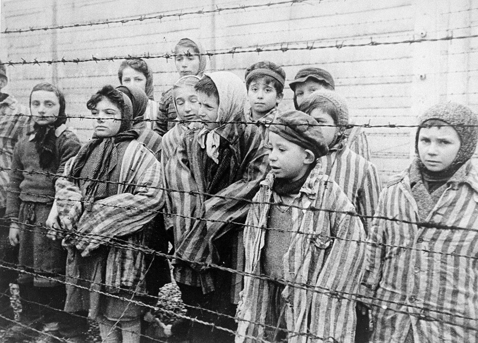 Enfants vêtus de vestes rayées de prisonniers derrière des barbelés