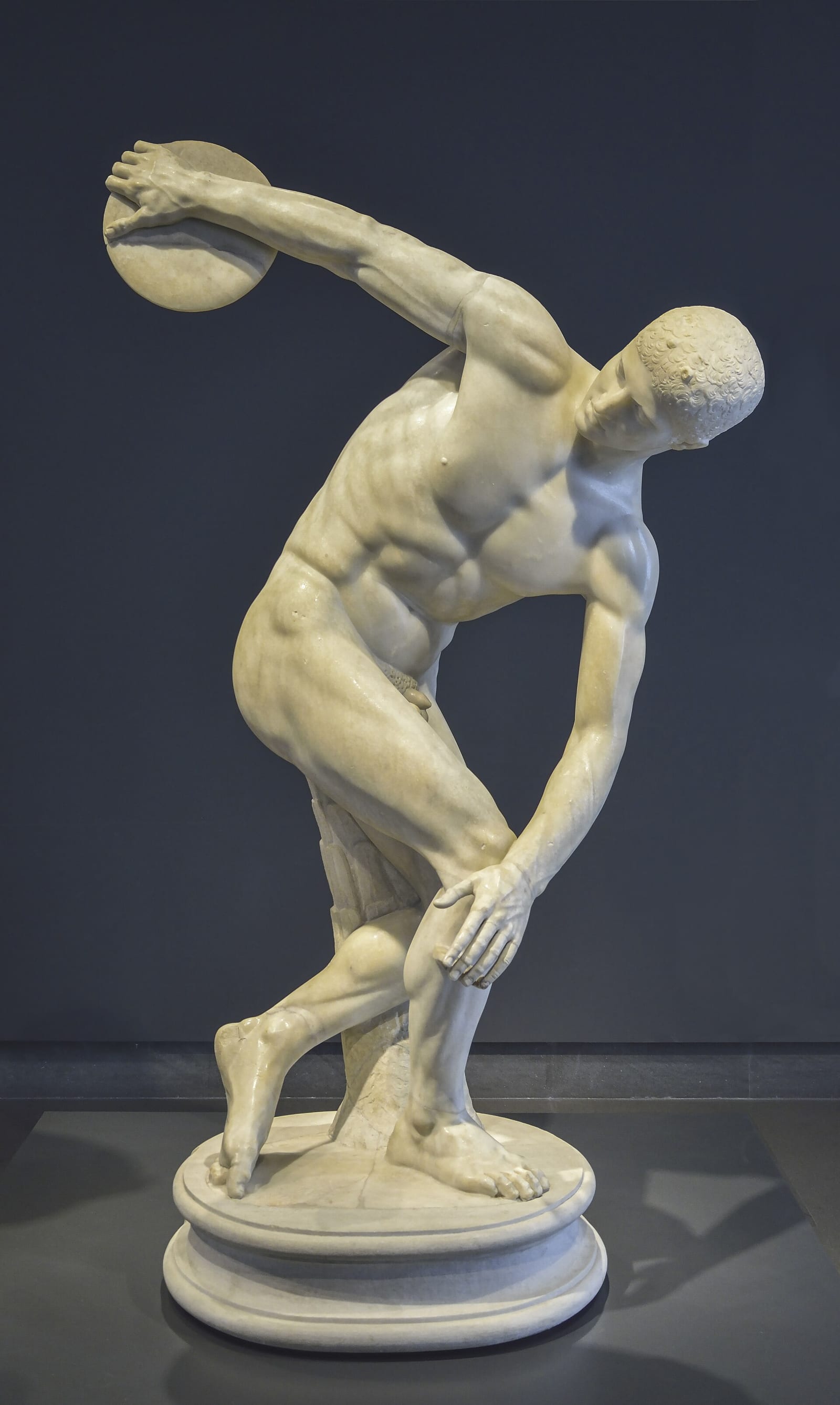 Statue de marbre d'un athlète nu ramassé sur lui-même, prêt à lancer le disque