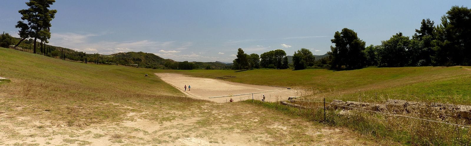 Longue piste de terre bordée de talus herbeux, sur le site antique d'Olympie