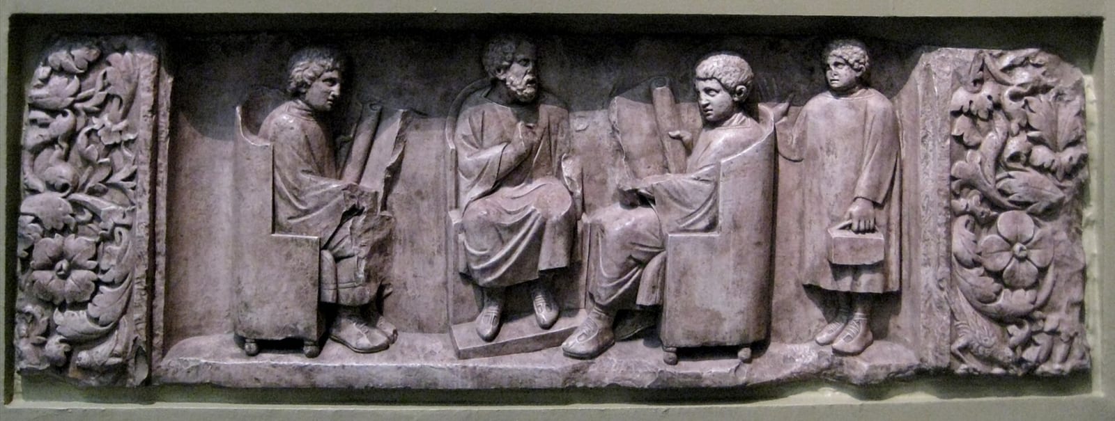 Relief antique montrant un maître assis et deux élèves tenant des rouleaux