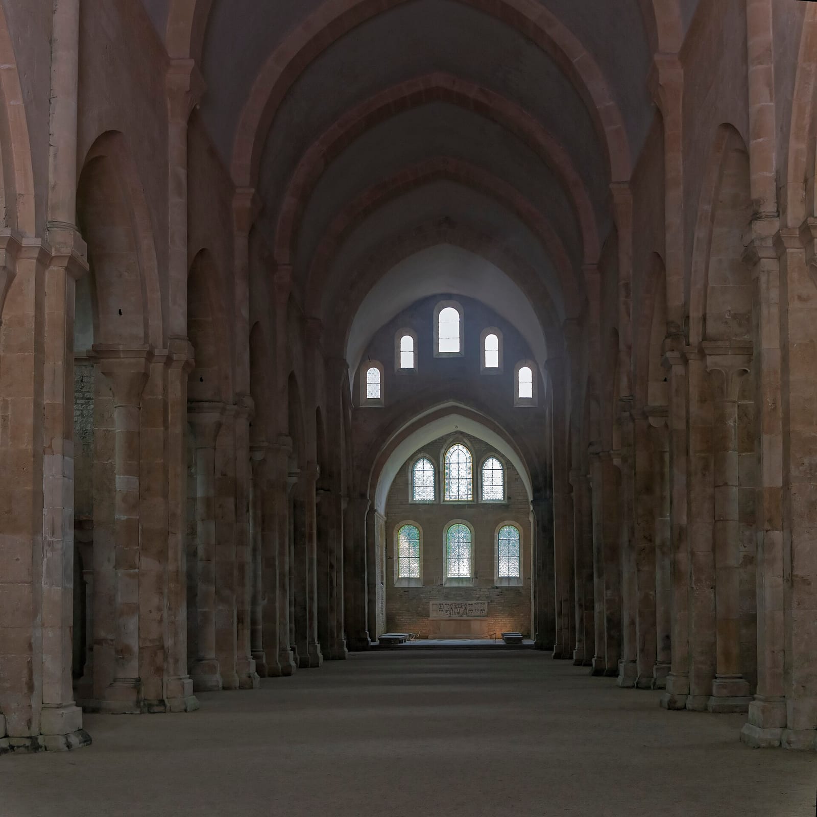 Nef d'église en pierre claire couverte d'une voûte en berceau, éclairée par de rares fenêtres