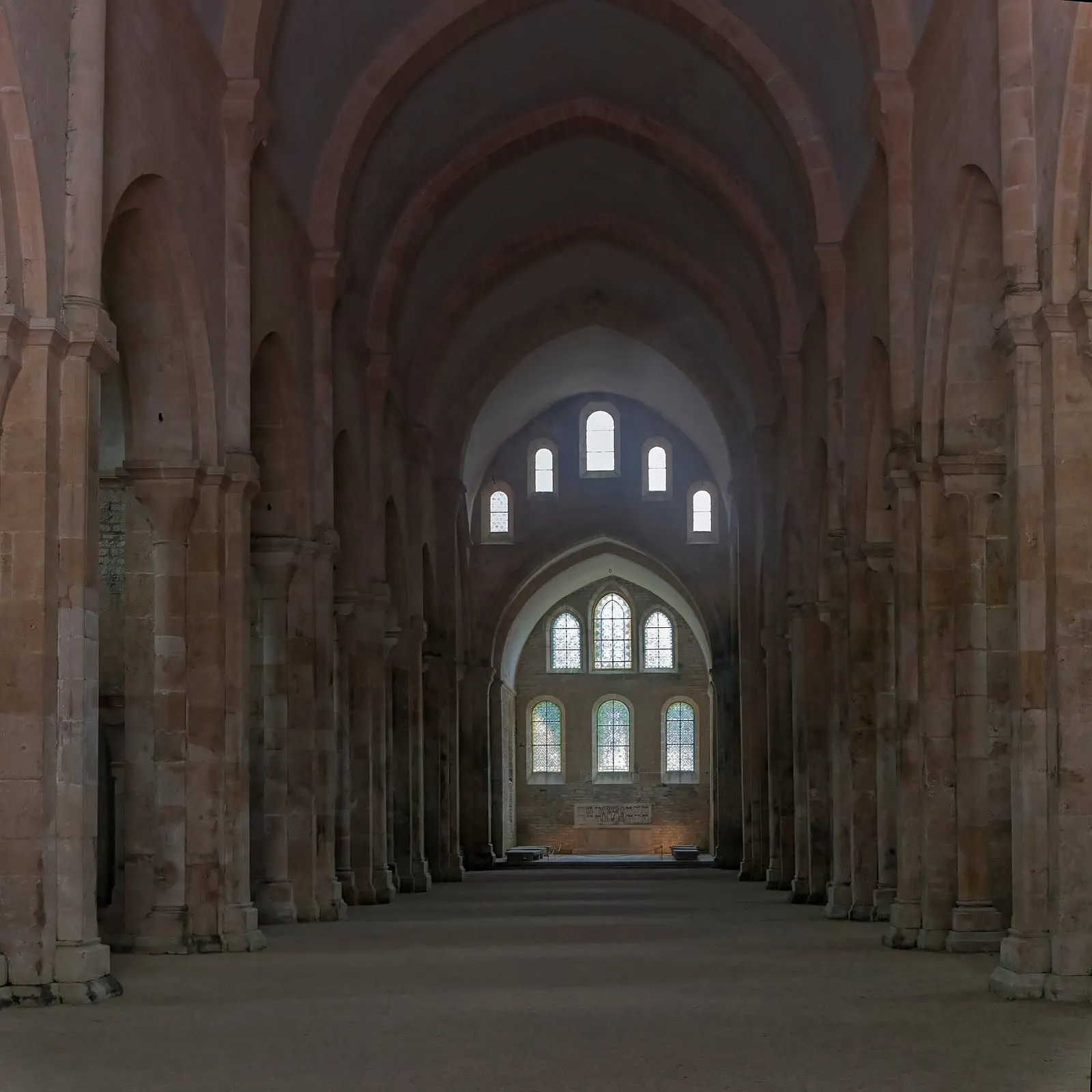 Nef d'église en pierre claire couverte d'une voûte en berceau, éclairée par de rares fenêtres