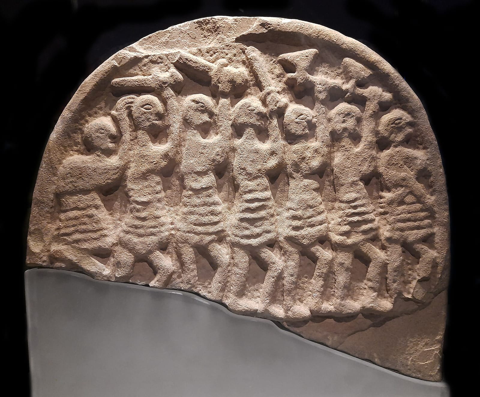 Bas-relief en pierre montrant une file de guerriers brandissant haches et épées