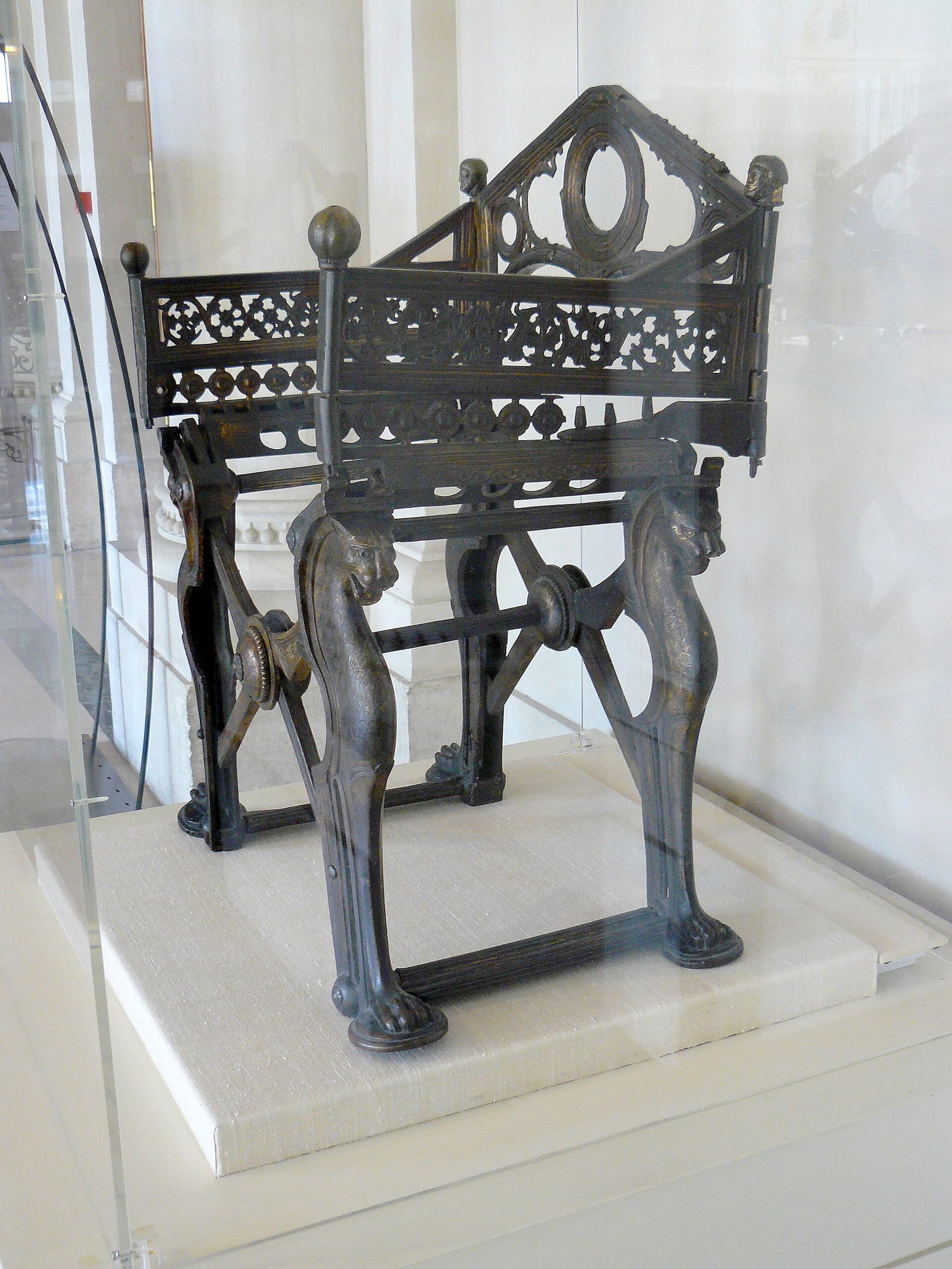 Siège pliant en bronze aux pieds en forme de pattes d'animal, dans une vitrine de musée