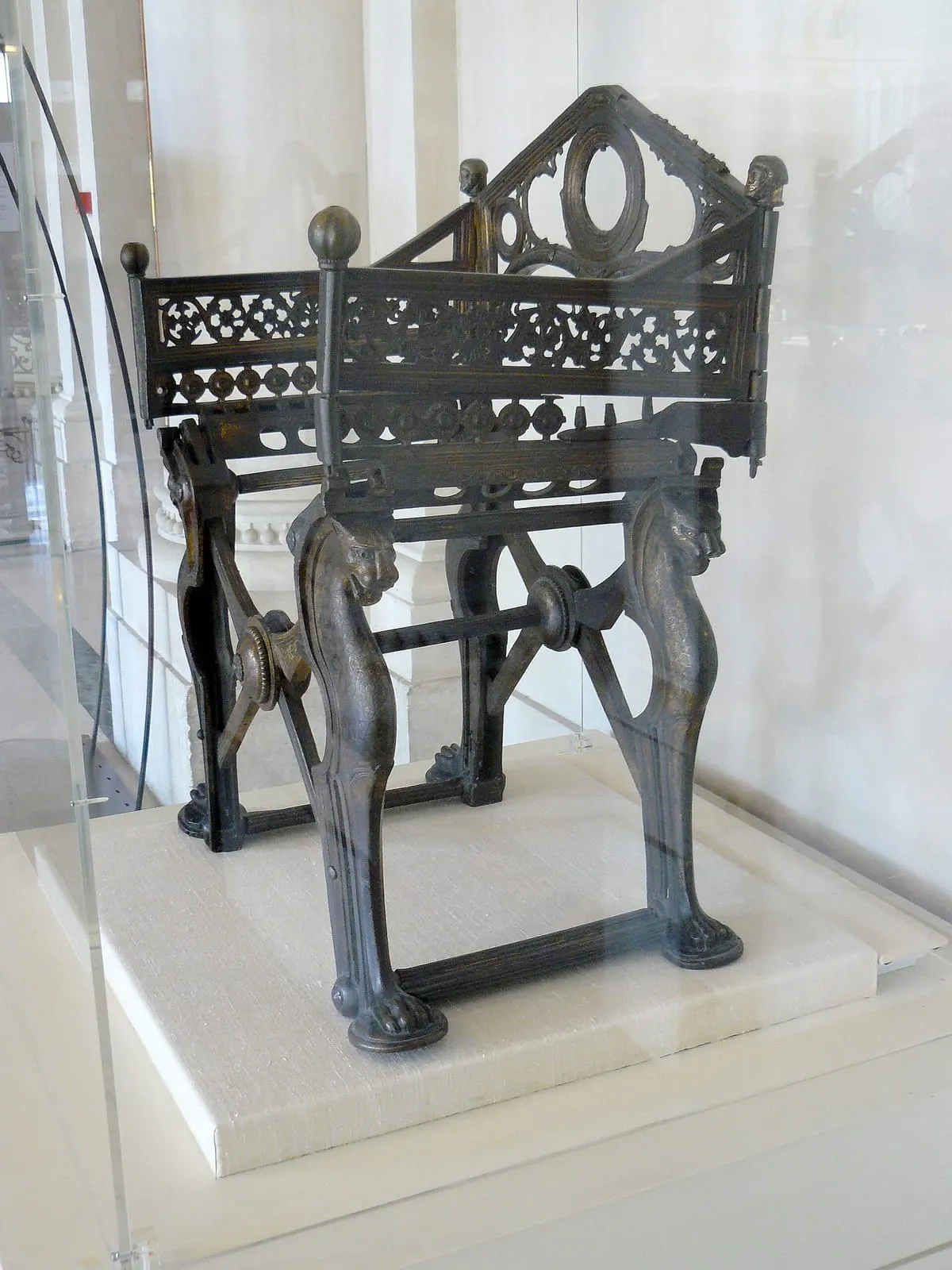 Siège pliant en bronze aux pieds en forme de pattes d'animal, dans une vitrine de musée